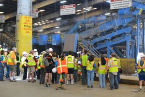 A tour group in hard hats and safety vests touring the Recycling Center at MSS
